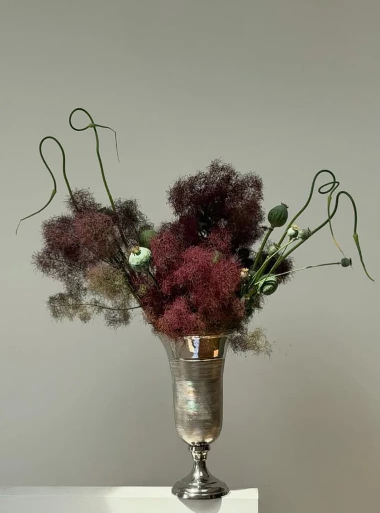 Smoky burgundy foliage in a silver vase with curved stems