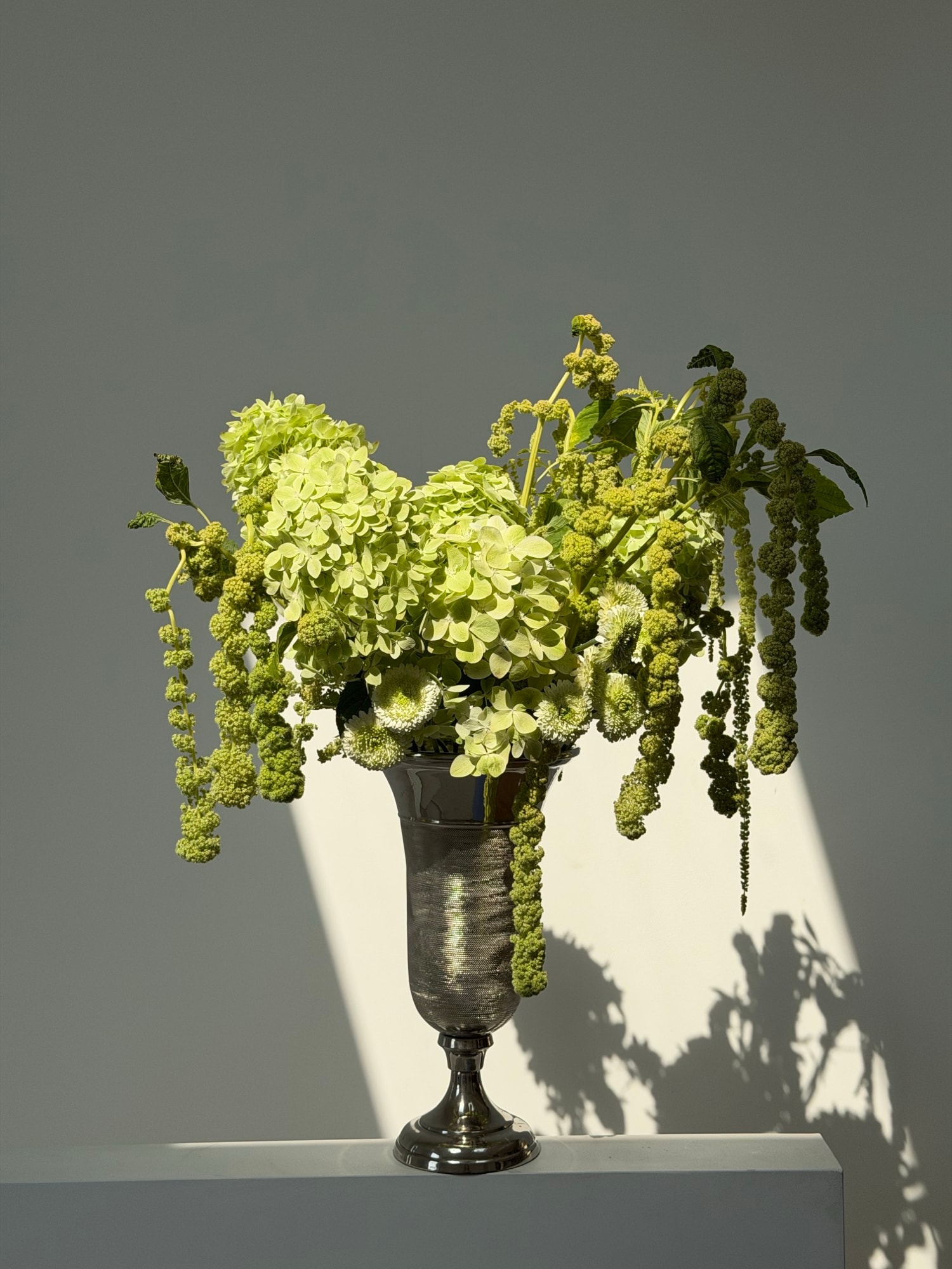 Monochrome green hydrangeas and trailing amaranthus in a dark metallic chalice vase
