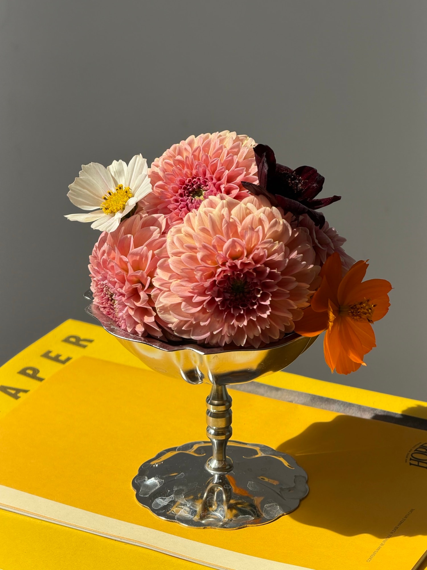Peach dahlias and cosmos in silver bowl on bright yellow book